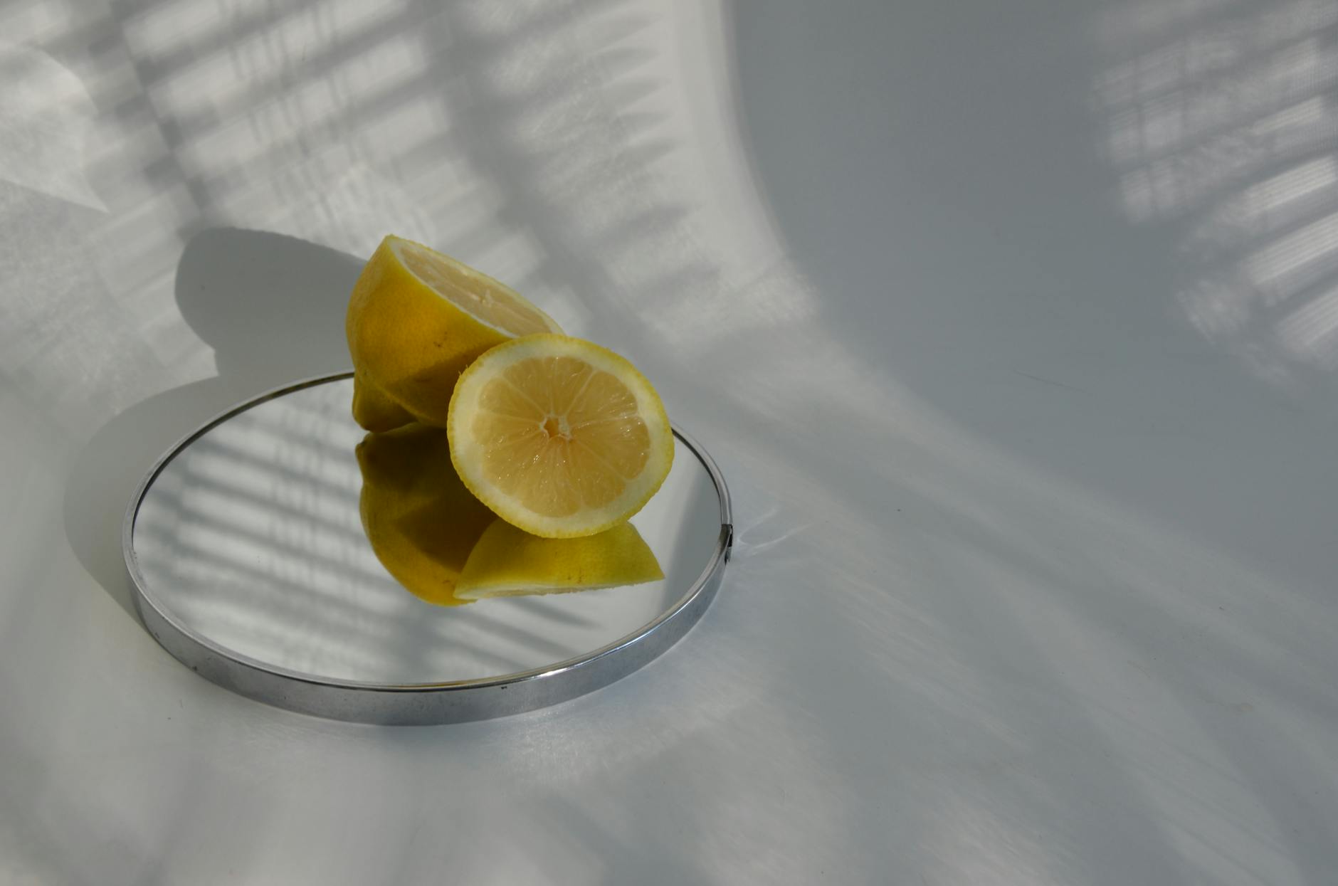 A hand with white nails holding a fresh lemon on soft pink background with additional lemons nearby, symbolizing renewal and fresh starts.