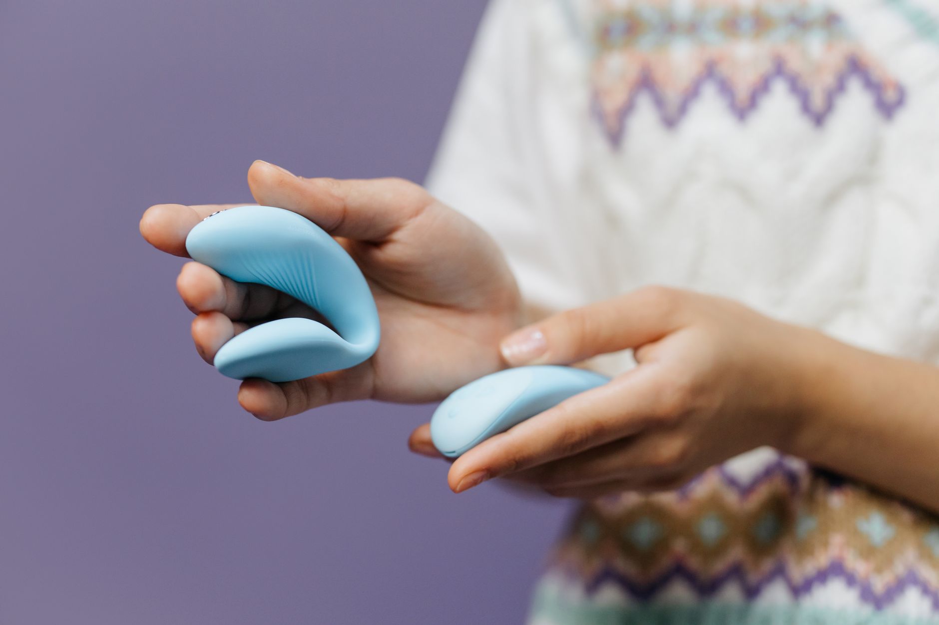 Close-up of hands holding a blue lemon vibrator against a purple background