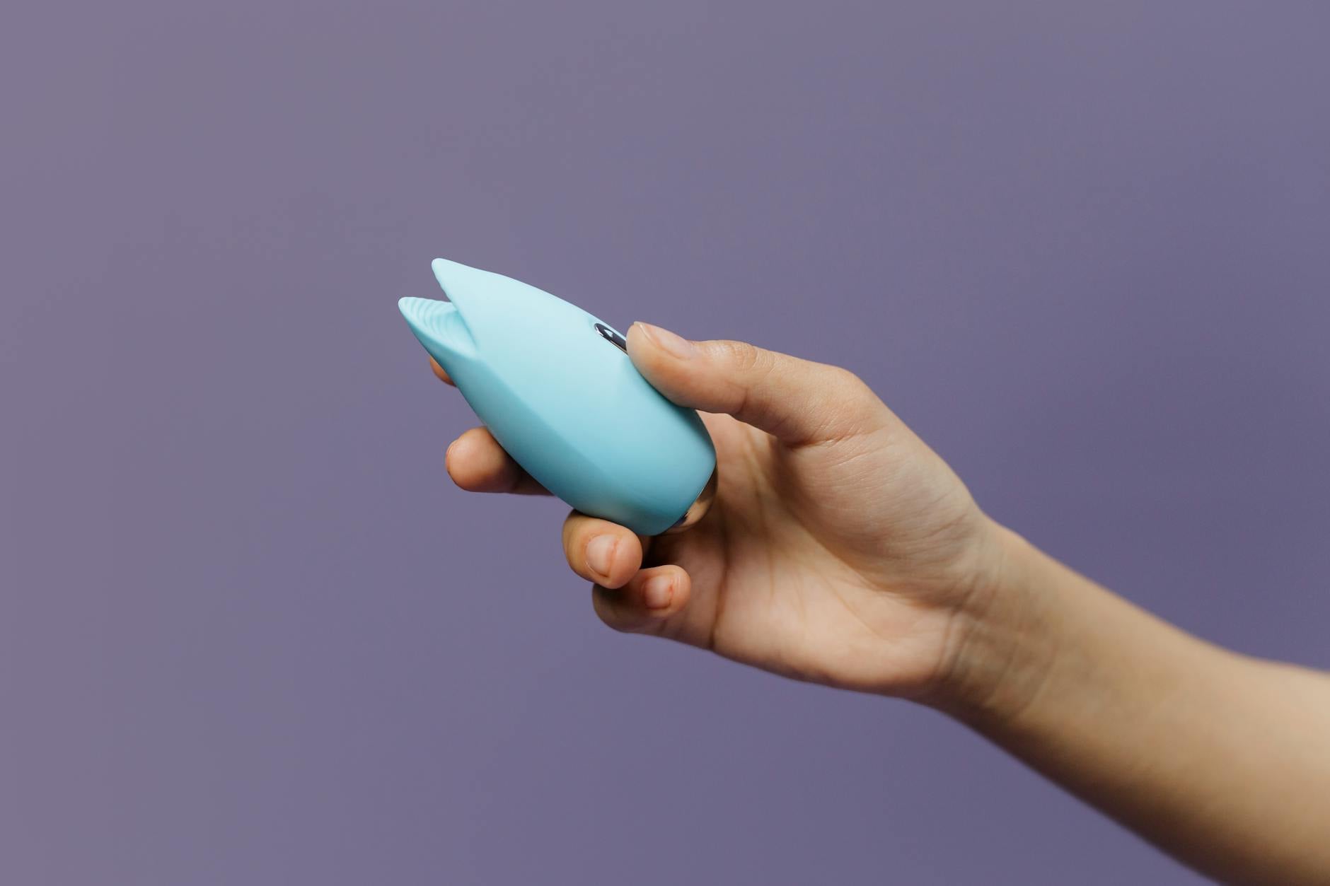 A hand holding a blue lemon clitoral vibrator against a purple background, representing sensuality and self-discovery.